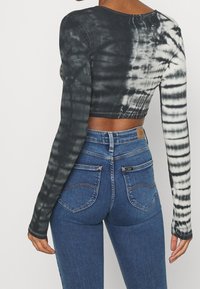 Der verkürzte Langarmshirt hat ein Batikmuster in Schwarz und Weiß. Kombiniert mit hoch taillierten blauen Jeans. Stoff aus einem Baumwoll-Mischgewebe mit gerippter Textur.