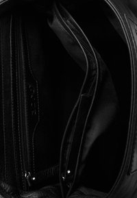 Interno di una borsa in pelle nera con più scomparti, incluso un taschino con zip. Fodera in tessuto morbido e dettagli in metallo visibili.