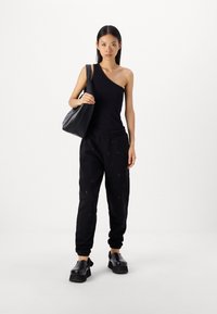 Svart axelbandslös linne ihop med svarta sweatpants med subtila mönster; modellen bär en svart handväska och har på sig klumpiga svarta skor.