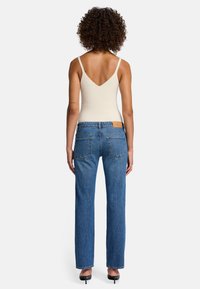 Canottiera a coste beige chiaro con scollo a V profondo, abbinata a jeans in denim blu medio a gamba dritta. I jeans presentano cuciture sottili e tasche.