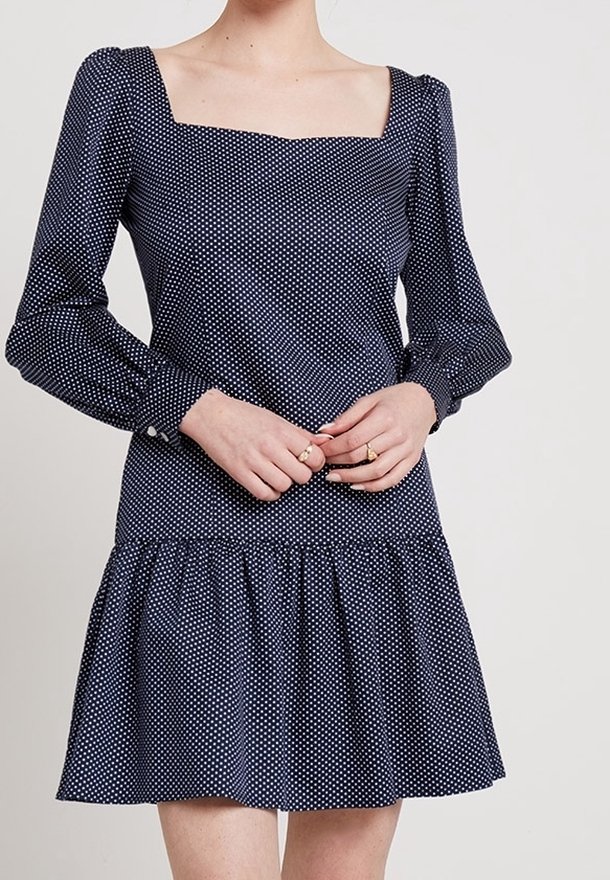 Vestido azul marino con lunares, escote cuadrado, mangas largas abullonadas, cuerpo ajustado y un dobladillo acampanado con volantes. Fabricado con una tela suave.