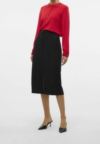Červená polokošile s dlouhým rukávem a límečkem na knoflíky, spárovaná s černou sukní střední délky s předním rozparkem a hladkým texturovaným materiálem. Černé vysoké podpatky.