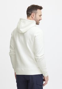 Sudadera blanca con capucha con cordón, puños acanalados y dobladillo. Textura suave, ajuste holgado y diseño minimalista. Combinada con pantalones cargo azul marino.