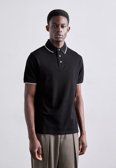 Polo shirt nera a maniche corte, con dettagli bianchi sul colletto e sui bordi delle maniche, e pattina con tre bottoni; realizzata in un tessuto liscio.
