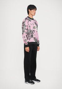 Felpa rosa con motivo floreale e di gabbie per uccelli nere; polsini e vita neri, abbinata a pantaloni neri e scarpe da ginnastica nere.