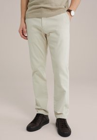 Light beige trousers made of soft fabric, featuring a slim fit, with a smooth texture and side pockets, paired with dark brown sneakers.