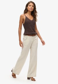 Top in maglia marrone con texture fantasia, scollatura a V, pantaloni beige a gamba larga e sandali con tacco marroni. Cintura accentuata in vita.