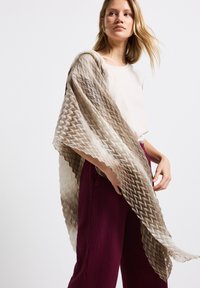 Écharpe légère aux tons dégradés de beige, ornée d'un motif géométrique et de plis texturés. Drapée sur un haut clair et un pantalon foncé.