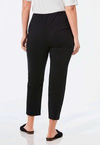 Pantalons noirs à taille élastique avec une coupe droite, longueur cropped et texture de tissu lisse. Portés avec des sandales noires à glissière.