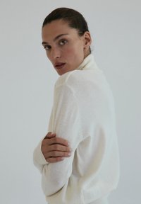 Kremowy sweter z golfem wykonany z miękkiej dzianiny, z prążkowanymi mankietami i pudełkowym krojem, eksponowany na neutralnym tle.