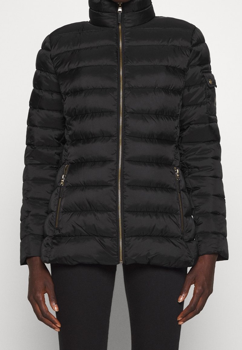 Svart, vadderad pufferjacka med dragkedja fram och dragkedjefickor, bärs av en person med mörk hud och svarta byxor.