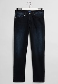 Mørke denimjeans med rett snitt, med frontlommer, knappestolpe og metallakenter. Stoffet har en glatt, noe falmet tekstur.