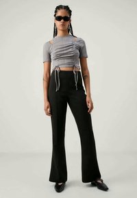 Crop top gris côtelé avec des liens sur les côtés, associé à un pantalon noir évasé. Les accessoires incluent des lunettes de soleil et des boucles d'oreilles créoles. Textures lisses tout au long.