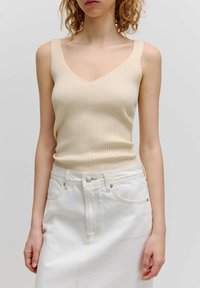 Beige geribbelde tanktop met een V-hals ontwerp en brede banden, gecombineerd met een high-waisted witte denim rok met contrasterende stiksels.