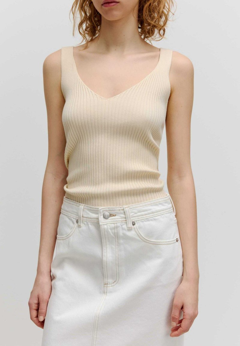 Beige geribbelde tanktop met een V-hals ontwerp en brede banden, gecombineerd met een high-waisted witte denim rok met contrasterende stiksels.