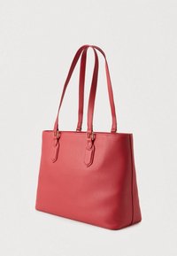 Punainen teksturoitu ostoskassi, jossa on kaksi pitkää hihnaa ja kullanväriset metalliosat, muotoiltu rakenne ja tasapohja.
