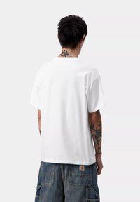 Biała bawełniana koszulka z okrągłym dekoltem i krótkimi rękawami, charakteryzująca się luźnym krojem. Noszona z ciemnoniebieskimi dżinsowymi szortami cargo.