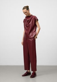 Top in faux leather borgogna con scollo drappeggiato, abbinato a pantaloni a gamba larga dello stesso colore, indossato con sneakers borgogna.