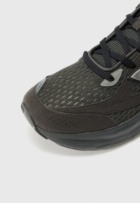 Baskets de sport noires avec une tige en tricot texturé et des accents en daim, une semelle rembourrée et des superpositions grises détaillées près des lacets.