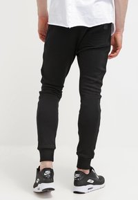 Černé sportovní tepláky s přiléhavým střihem, žebrovanými manžetami a zadní kapsou, spárované s černými sportovními botami s bílými detaily.