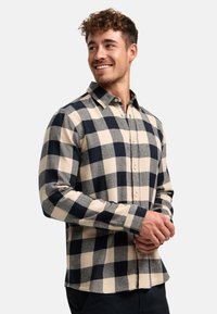 Kariertes Flanellhemd mit Knopfleiste, das ein großes Navy- und Beige-Karomuster zeigt. Lange Ärmel, Kragen und abgerundeter Saum. Weicher Stoff.