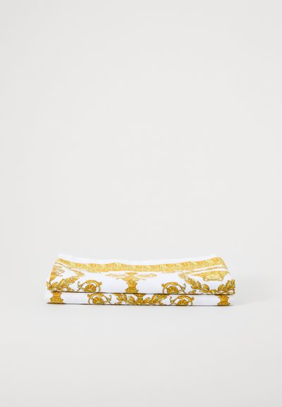 Material textil pliat, cu un fundal alb ce prezintă un model baroc auriu, incluzând detalii florale și ornamentale. Textură moale.