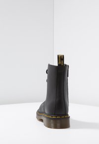 Musthave nahkasaapad, mis ulatuvad ankle'ist kõrgemale, ümmarguse varbaga, jalatsi tallal kollased õmblused ja taga tõmblint mugavaks jalga panemiseks.