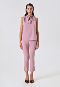 Blusa senza maniche rosa chiaro con un dettaglio a fiocco annodato, abbinata a pantaloni aderenti coordinati con dettagli di bottoni alle caviglie.