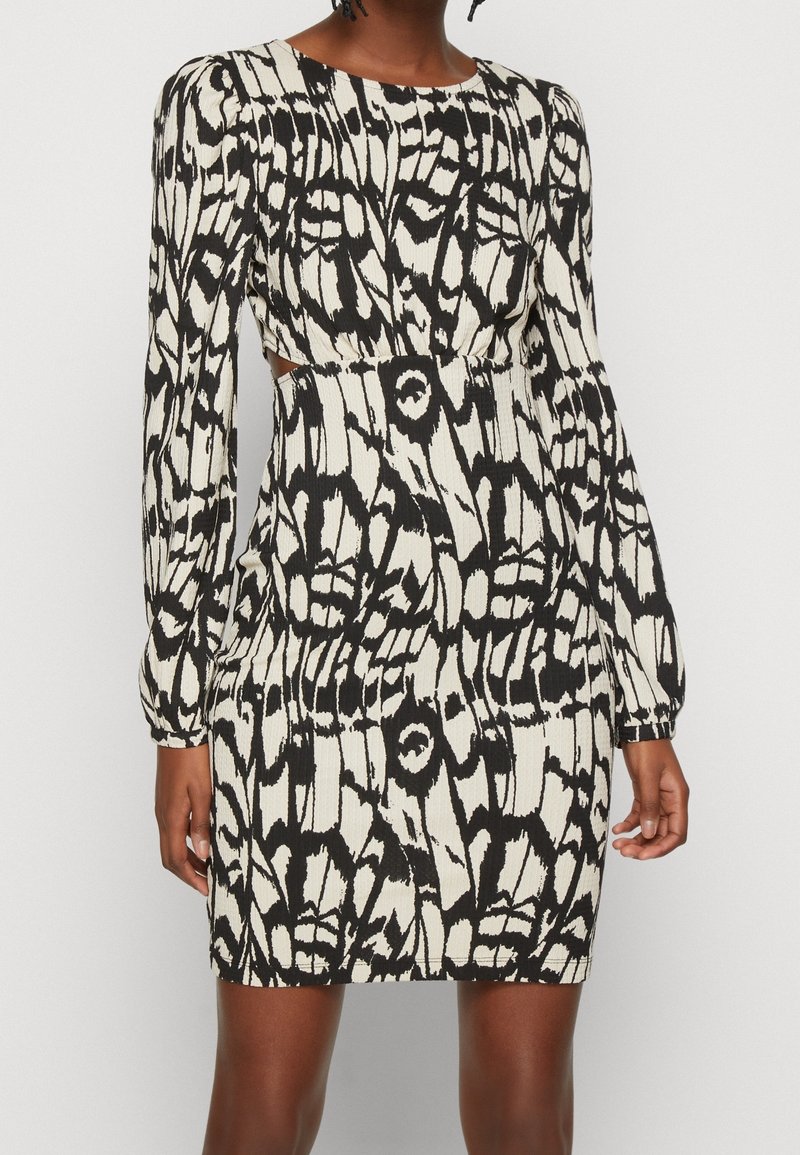 Robe à manches longues noire et blanche à motifs, avec une silhouette ajustée, un tissu texturé, un col rond et des découpes à la taille.