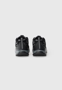 Pair of black athletic shoes with gray midsoles, viewed from the back on a white background, showing reflective heel pull tabs.