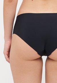 Fekete, magas derekú fürdőruha alsó, sima, rugalmas anyagból készült. Tiszta vonalú és minimalista dizájn jellemzi, amely különböző fürdőruha stílusokhoz is megfelelő.