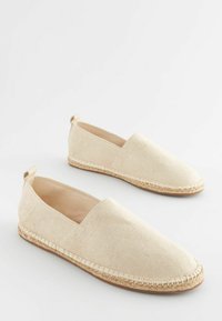 Beige canvas espadrilles with a slip-on design, featuring a jute sole and stitching detail along the border. Smooth texture throughout.