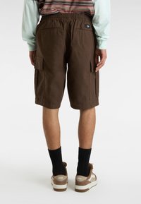 Brązowe szorty cargo z elastycznym pasem, dwoma bocznymi kieszeniami i kieszeniami z tyłu, w połączeniu z brązowo-białymi trampkami i czarnymi skarpetkami.