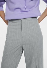 Šedé pruhované kalhoty s dobře padnoucím střihem a jemnou texturou. Stylovány s fialovou mikinou, která má akcent s táhlem.