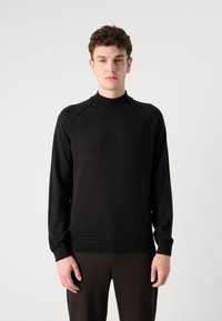 Schwarzer gestrickter Pullover mit hohem Kragen, langen Ärmeln und Raglan-Design. Das Material scheint weich mit einer glatten Textur und minimaler Detailgestaltung zu sein.