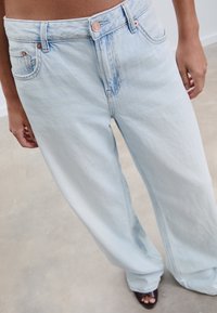 Svetlo modri široki jeans iz denima, z copper gumbi in stranskimi žepi. Gladka tekstura z sproščenim krojem.