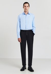 Camicia button-up azzurro chiaro con maniche lunghe, pantaloni neri e scarpe di pelle nera. Vestibilità slim, texture liscia e senza motivi visibili.