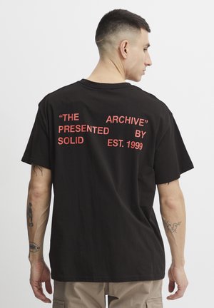 Black cotton T-shirt with short sleeves, featuring red text on the back: “THE ARCHIVE” “PRESENTED BY SOLID EST. 1999.”