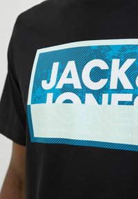 Sort bomulds T-shirt med et iøjnefaldende hvidt og blåt grafik med teksten "JACK & JONES" og stribede detaljer i blå og aqua.