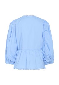 Blusa peplum azzurro chiaro con maniche a sbuffo, dettaglio con orlo a scallop e una texture di cotone morbida. Vista posteriore con vita arricciata.