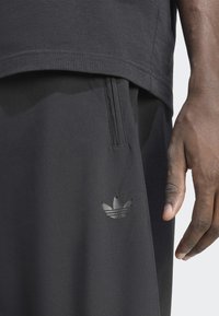 Juodi sportiniai šortai iš lygaus audinio su subtiliu blizgesiu. Turi siuvinėtą kišenę, prigludusią liemenėlę ir atspindinčią logotipą.