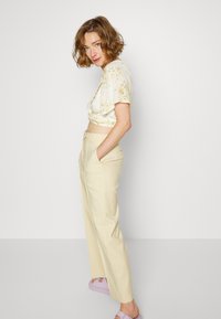 Top cropped floral creme, calças beje de cintura alta e sandálias de plataforma lavanda. Tecido macio com um discreto padrão de flores.