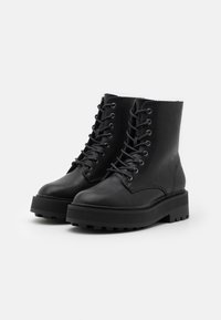 Botas de cuero negro hasta el tobillo con punta redonda, cordones en la parte delantera y suela de plataforma gruesa con ranuras texturizadas. Acabado liso y acentos mínimos.