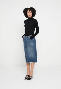 Top nero a maniche lunghe abbinato a una gonna midi in denim blu con orlo sfrangiato. Indossato con tacchi neri a punta.