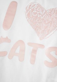 Biała tkanina z różowym nadrukiem zawiera tekst "Kocham KOTY" oraz stylizowaną grafikę kota, wszystko w zabawnym, wyraźnym kroju czcionki.