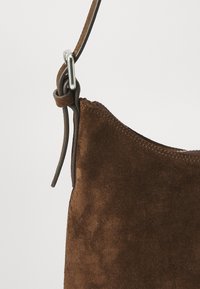 Brauner Wildleder-Handtaschenriemen mit silberner Schnalle und Schlaufen-Detail auf einem schlichten hellen Hintergrund.
