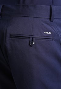 Mörkblå byxor med en stilren design, slät yta, en bakficka med knapp och en broderad "RLX"-logotyp på sidan.