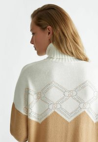Maglione lavorato a maglia con colletto alto, parte superiore color crema e parte inferiore color sabbia, decorato con ricami geometrici e dettagli.