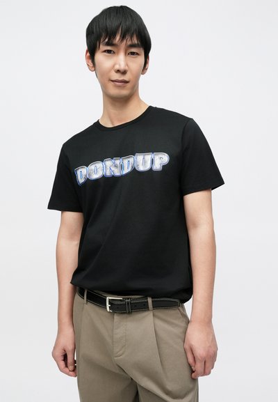 Μαύρο βαμβακερό t-shirt με μεγάλο μεταλλικό μπλε τύπωμα "DONDUP" στο στήθος, συνδυασμένο με χακί παντελόνι και μαύρη ζώνη.