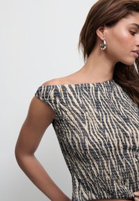 Top cu umeri descoperiți, realizat dintr-un material texturat cu un model în zigzag în culori de albastru închis și crem. Prezintă o siluetă ajustată și mâneci scurte.